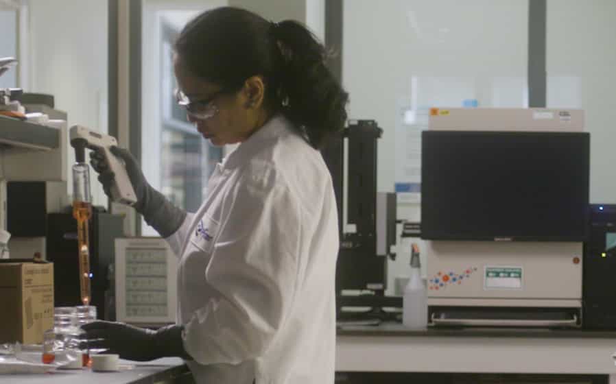 Woman with brown hair and wearing a white coat in the lab, working on vaccine research